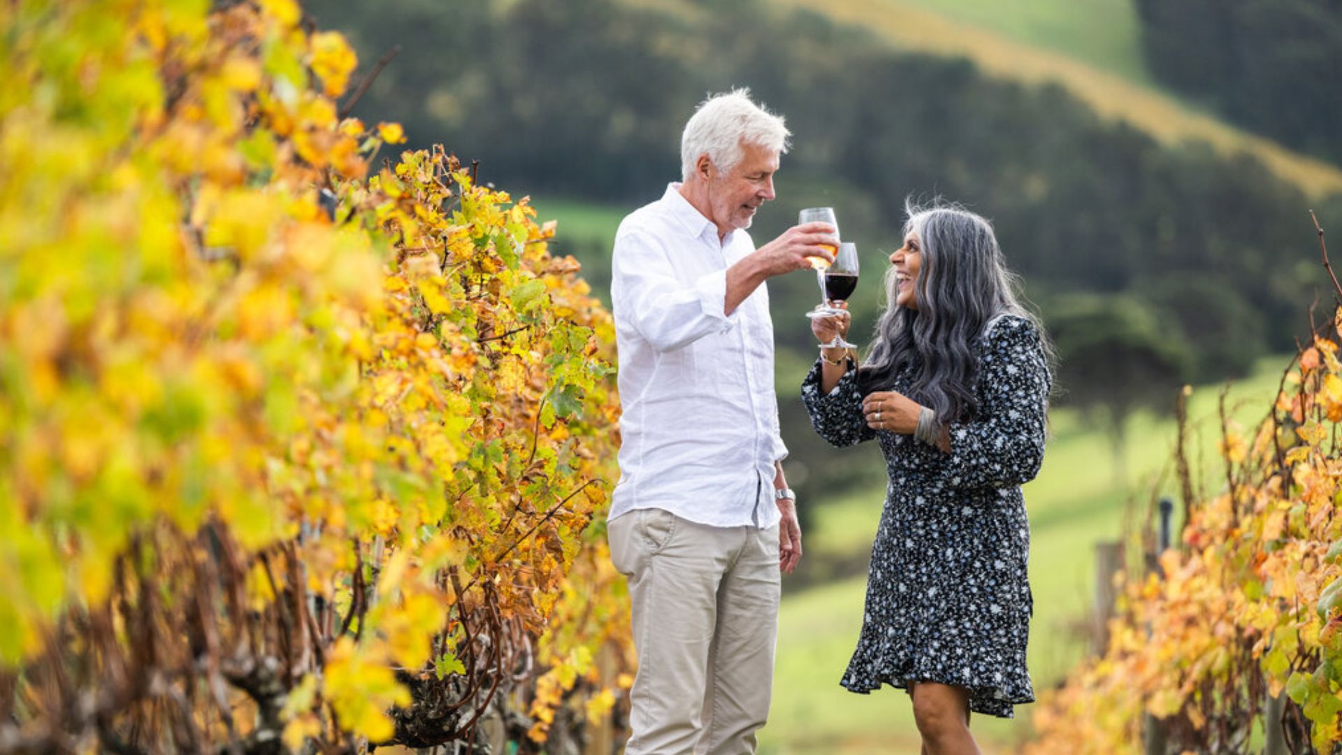 Couple enjoying wine tasting among autumn vineyards on Waiheke Island during ANZAC weekend getaway.
