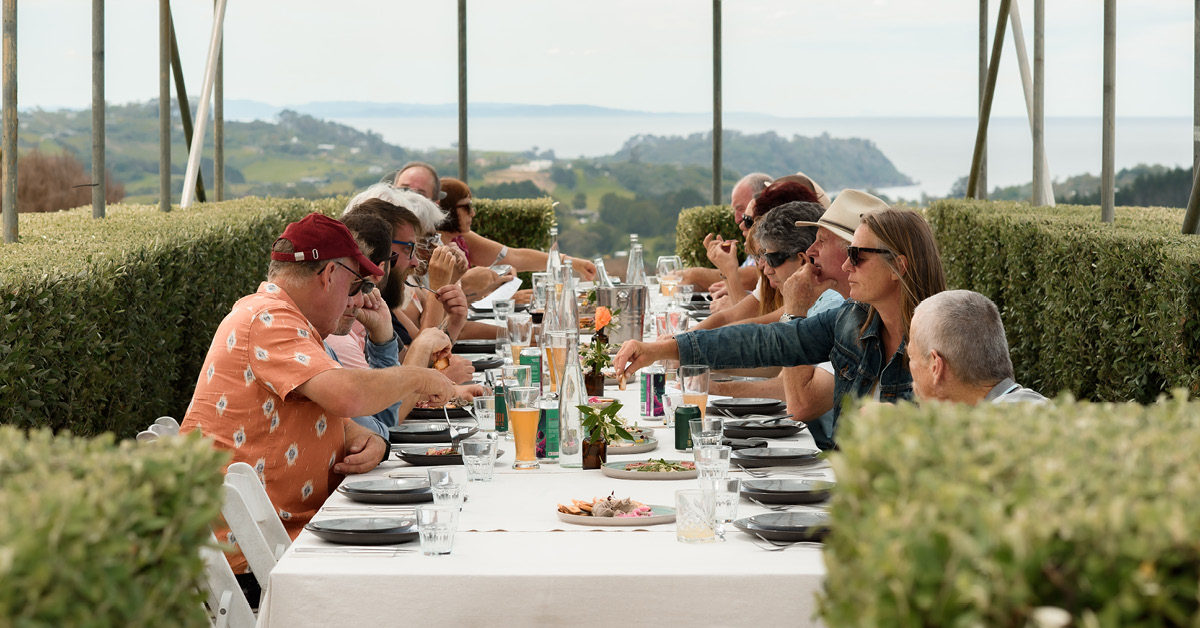 Group dining at a long outdoor table with Hauraki Gulf views on Waiheke Island